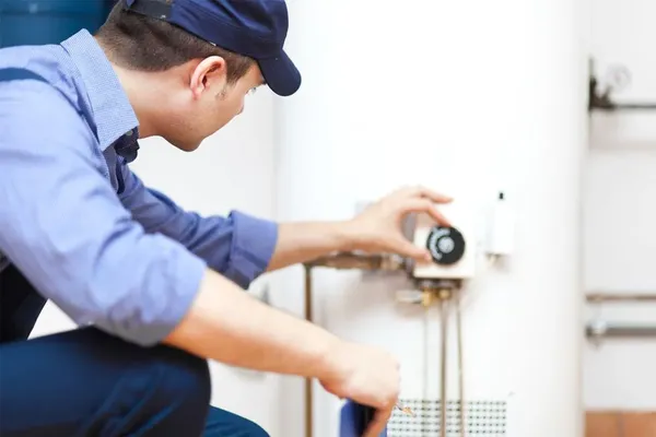 a plumber in a blue shirt kneeling, servicing a water heater unit, emphasizing plumbing repairs and installations in Franklin County